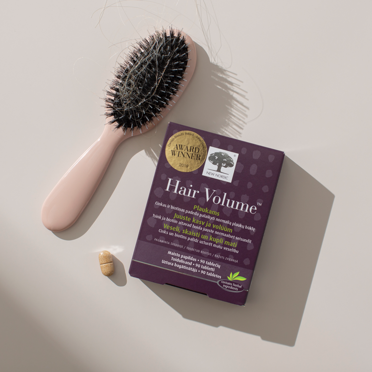 New Nordic Hair Volume™ maisto papildas šalia plaukų šepečio su plaukais ir tabletės.