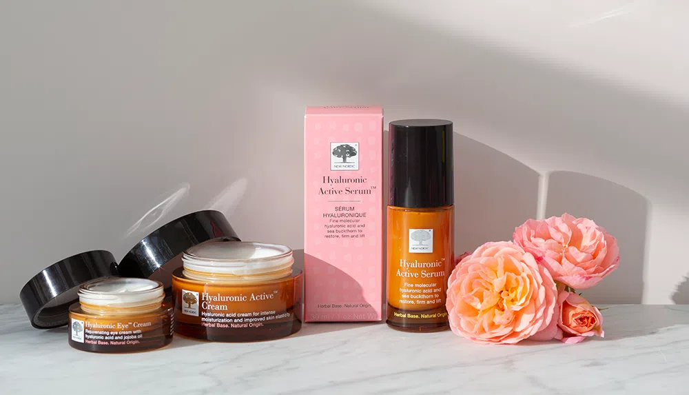 keletas mūsų „Hyaluronic Active“ buteliukų ir dėžutė su rožine dėžute bei rožine gėle
