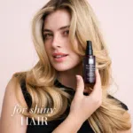 Moteris su gražiais plaukais, laikanti „Hair Volume™ Shine Serum“ buteliuką su užrašu „Blizgiems plaukams“.