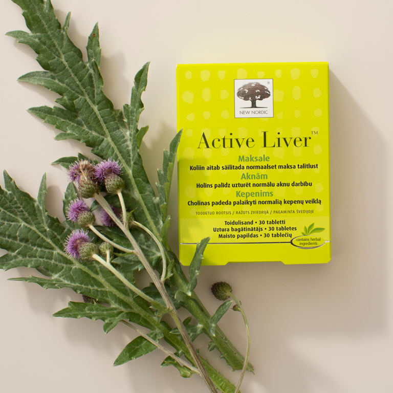 „New Nordic Active Liver“ pakuotė šalia margainio lapų ir violetinės spalvos žiedų.