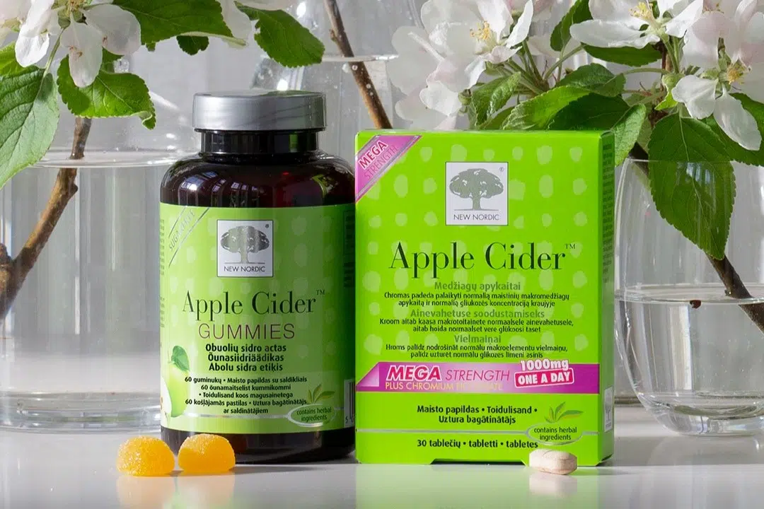 New Nordic Apple Cider™ Gummies ir Apple Cider™ maisto papildai su guminukais ir tablete, apsupti žydinčių šakų.