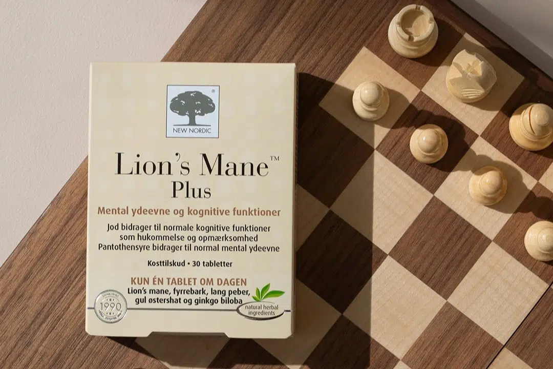 New Nordic Lion’s Mane™ Plus maisto papildas šalia medinės šachmatų lentos su figūromis.